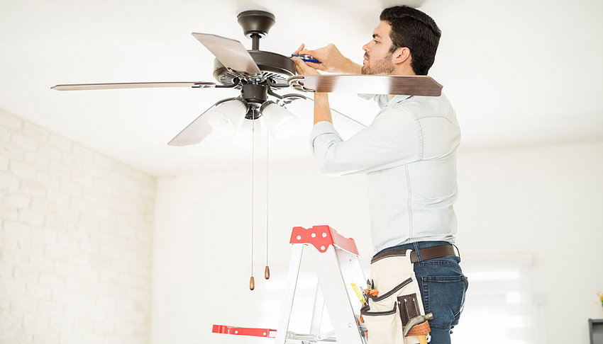 Our electrician repairing a ceiling fan in the living room while standing on a ladder. Licensed Electrician Suttons Bay MI